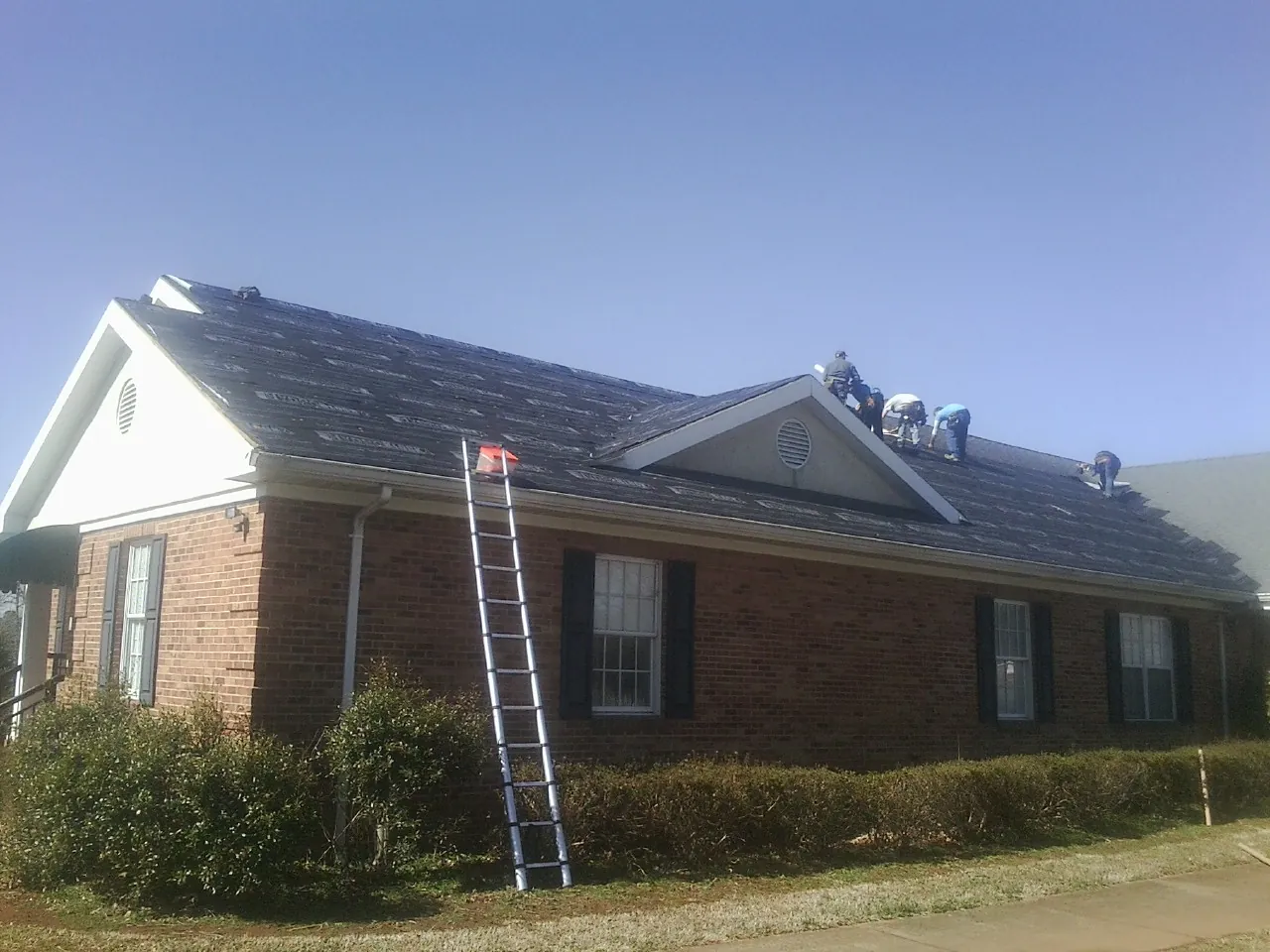 Crew tearing shingles off a brick ranch roof with a ladder set — Metal Roof Repair work by our crew in Woodsfield