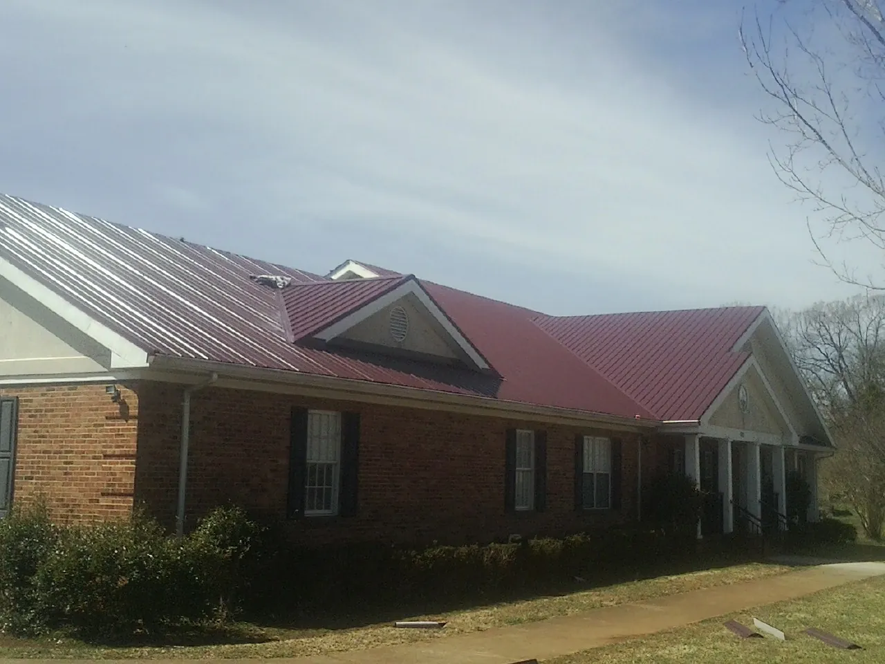 Red metal roof with gabled entries on a long brick building, from a Hail Damage Roof Repair job in Woodsfield