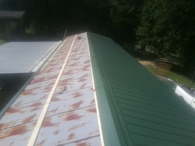 Old rusted panels beside newly installed green metal roofing — Wind Damage Roof Repair by Roofing Brothers in Woodsfield