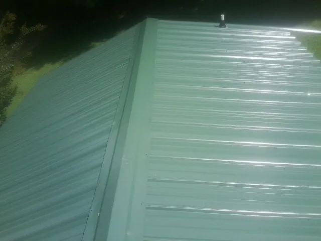 New green metal panels meeting at the ridge of a roof — Flat Roof Repair work by our crew in Woodsfield