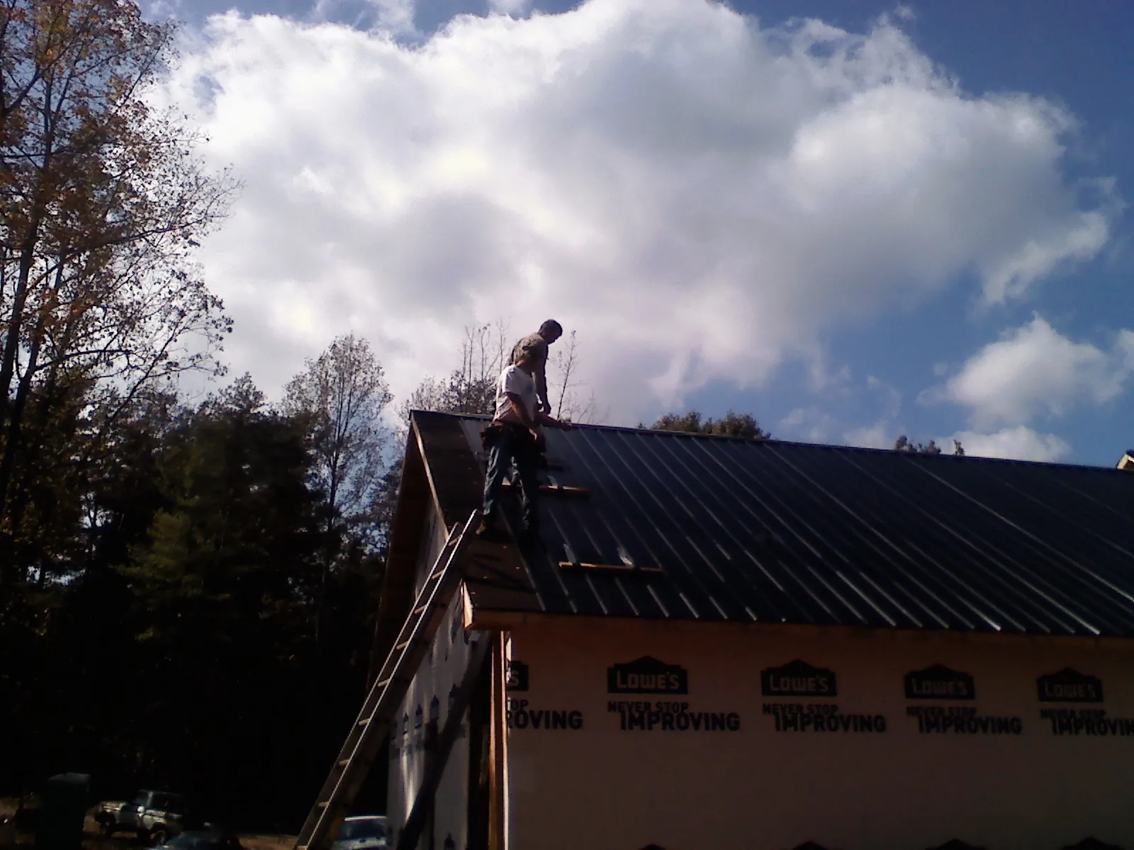 Roofer fastening dark metal panels high against a cloudy sky, from a Roof Inspection job in Woodsfield