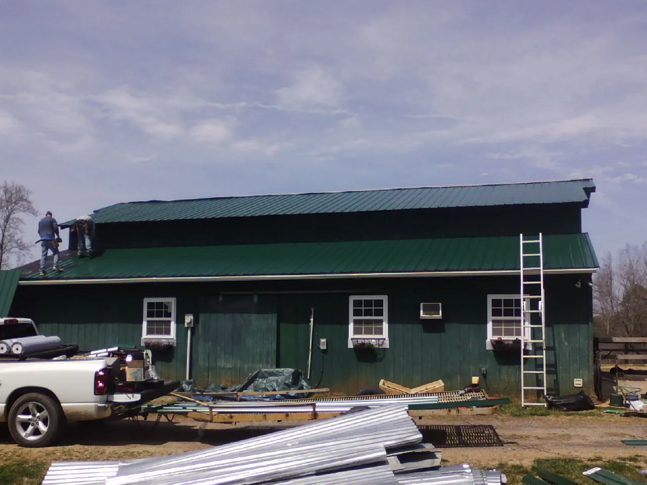 Crew installing green metal roofing on a large green barn in Woodsfield