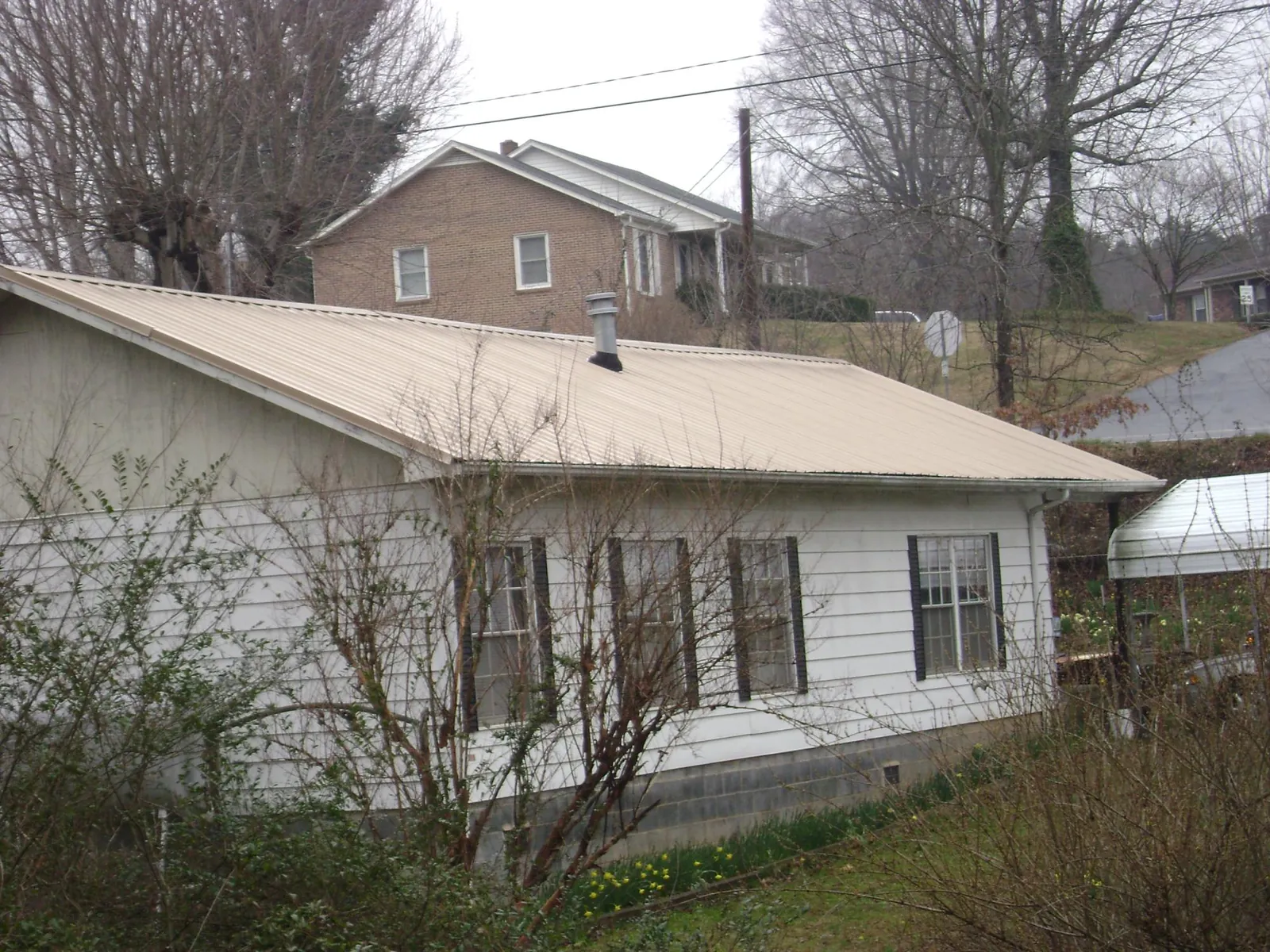 Tan metal roof on a white sided house set into a hillside — Commercial Roofing by Roofing Brothers in Woodsfield
